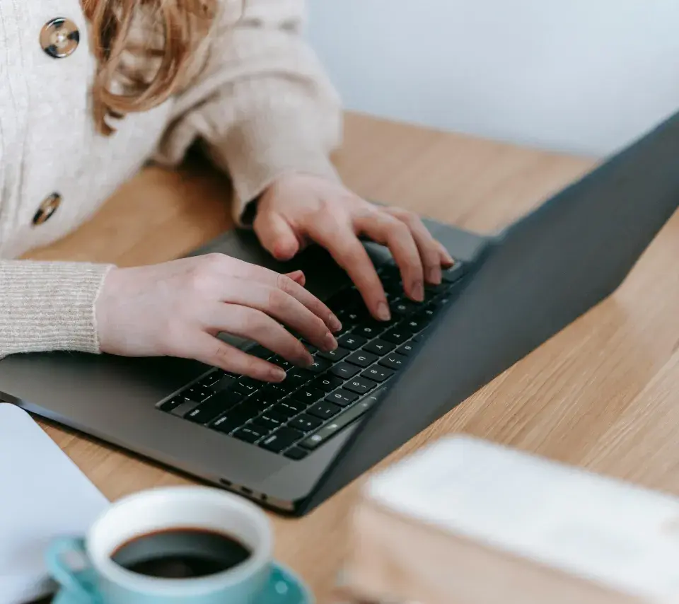 Une personne rédige sur un ordianteur un texte avec une tasse de café prs d'elle